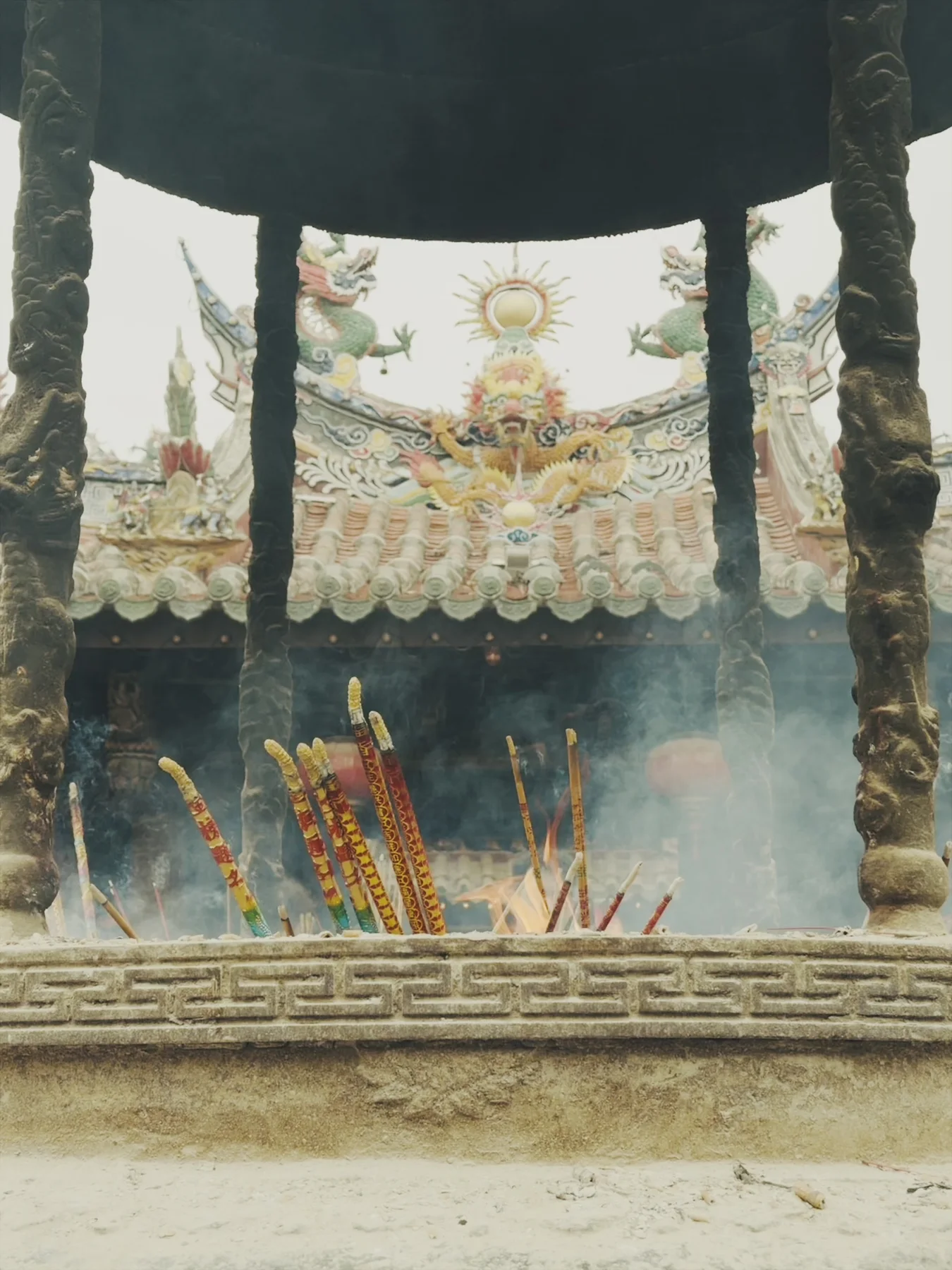 Incense sticks pass through smoke at Guanyue Temple, while a bright ceramic sun and roof ornament appear beyond the doorway