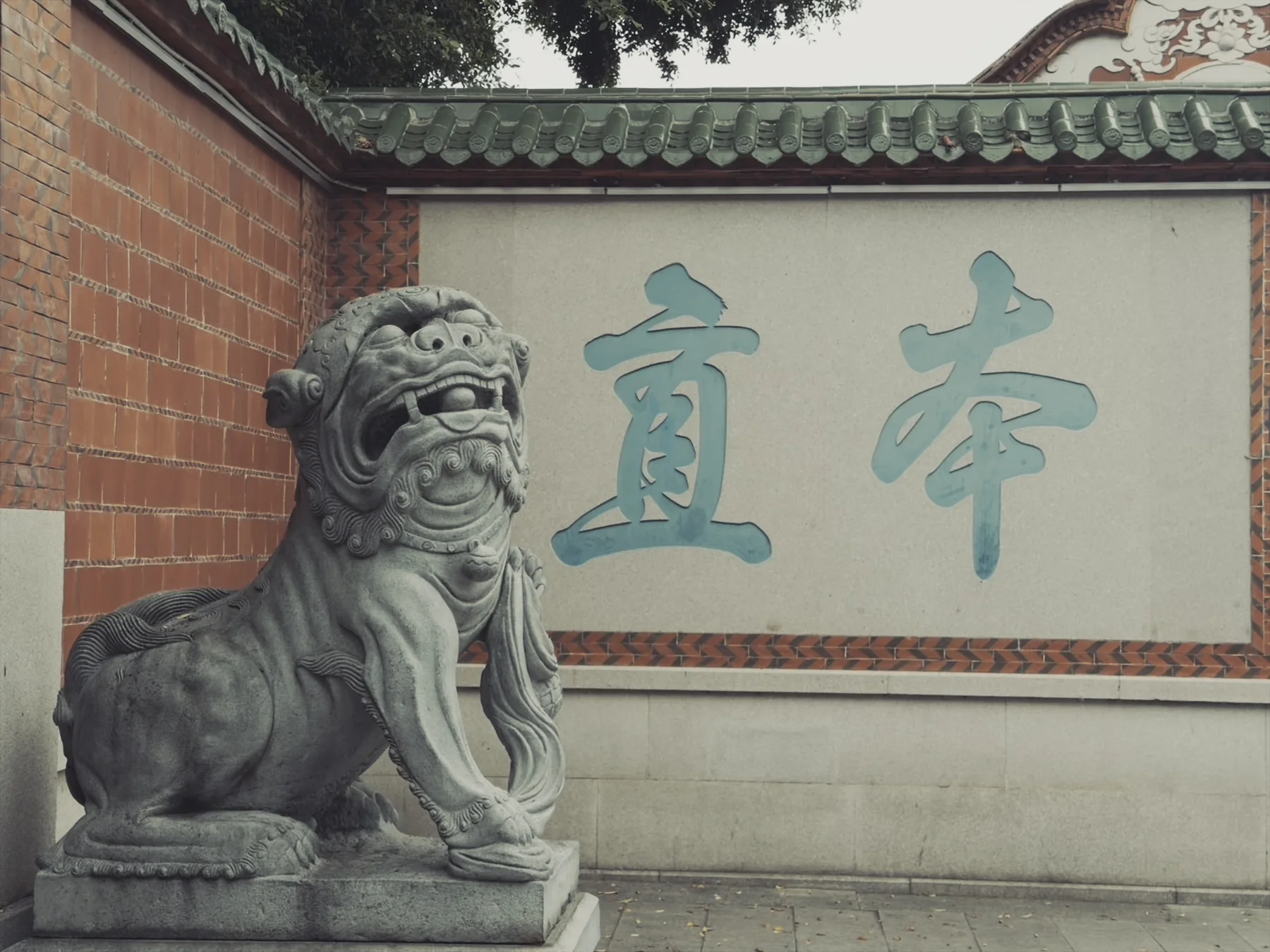 The pale wall at Qingjing Mosque inscribed with the Chinese characters for “Revere Heaven,” beside grey stone lions, red brick, and green roof tiles