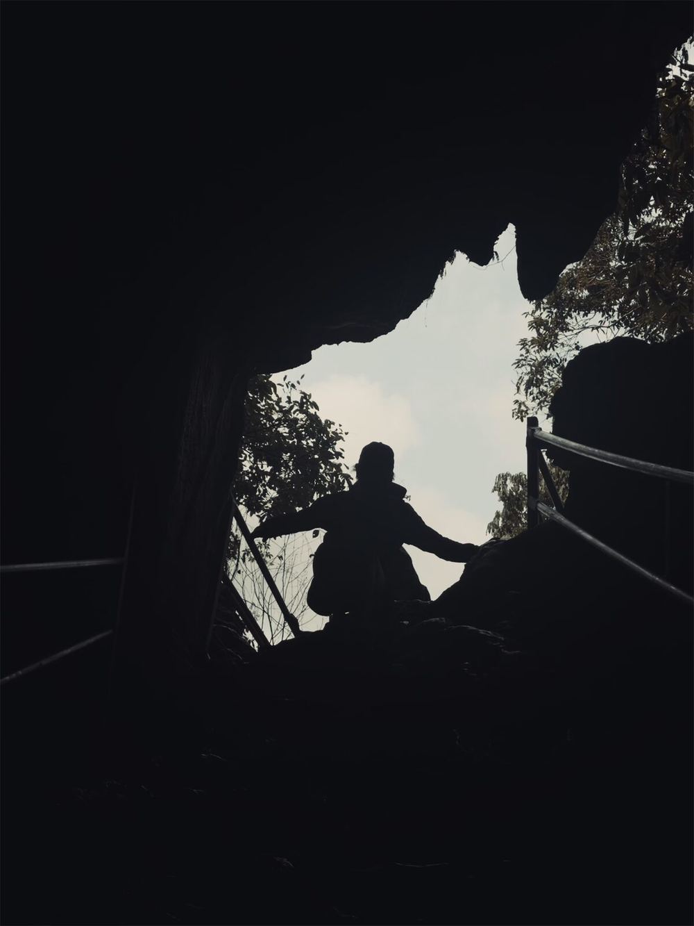 Looking up at the mouth of a cave: the silhouette of a hiker against the bright sky — the light is outside, the darkness is at your feet, and the body is just about to walk in