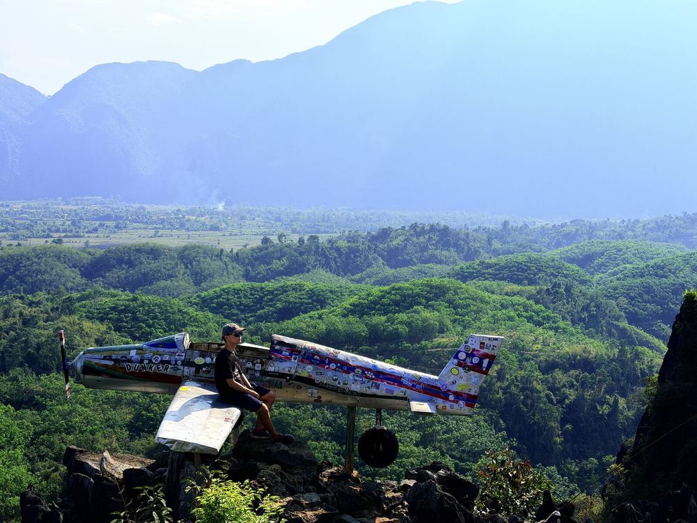 The &ldquo;Dunker&rdquo; plane installation on top of Nam Xay mountain in Vang Vieng — covered in stickers from travelers around the world, with layer after layer of karst mountains and rice paddies behind it. A joy already certified by the footsteps of countless strangers